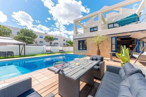 A pool area with a table and chairs, a lounge chair, and a building with a balcony. - Villa Lucentum (Alicante)