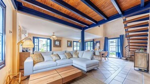 A spacious living room with a light-colored sectional sofa, a wooden coffee table, and a dining area with a small table and chairs. - Villa Lucentum (Alicante)