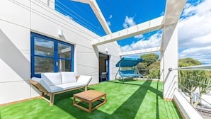 A balcony with a white sofa, a wooden table, and a blue umbrella. - Villa Lucentum (Alicante)