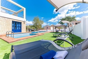 A poolside area with a lounge chair, a small pool, and a building with a blue door. - Villa Lucentum (Alicante)