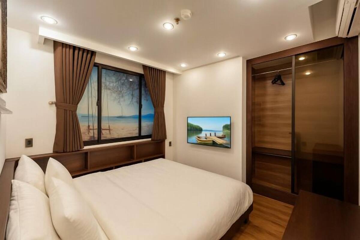 Un dormitorio con cama, ventana con cortinas, televisor montado en la pared y armario.