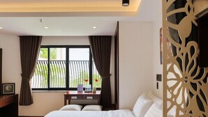 Une chambre d’hôtel comprenant un lit, un bureau, une fenêtre avec des rideaux et un élément de séparation décoratif.