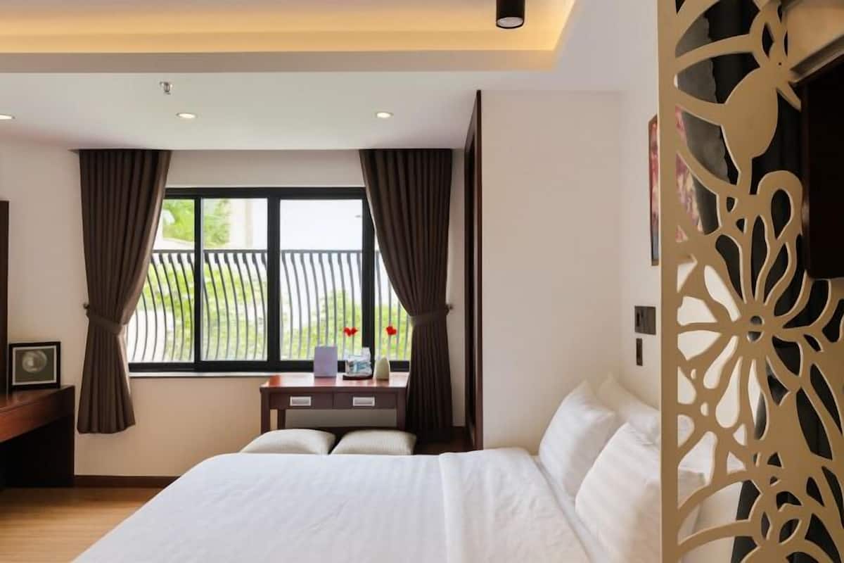 Una habitación de hotel con una cama, un escritorio, un ventanal con cortinas y un separador decorativo.
