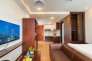 Ein modernes Hotelzimmer mit Flachbildfernseher, einer Couch, einem Esstisch mit Pflanze und einer Küchenzeile im Hintergrund.