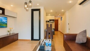 Un salon moderne avec un canapé, une table basse sur laquelle sont posées des boissons, un téléviseur et un couloir menant à la cuisine.