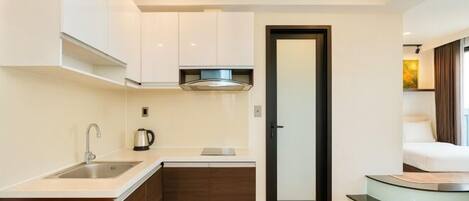 A compact kitchen with a sink, stove, and cabinets, leading to a bedroom with a glass staircase.