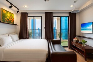 Una habitación de hotel con cama, zona de estar, televisión y balcón con cortinas.