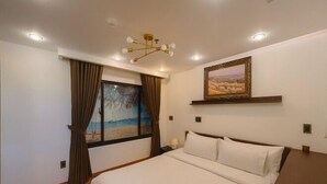 Une chambre à coucher avec un lit, une fenêtre avec des rideaux, un tableau au mur et un luminaire au plafond.