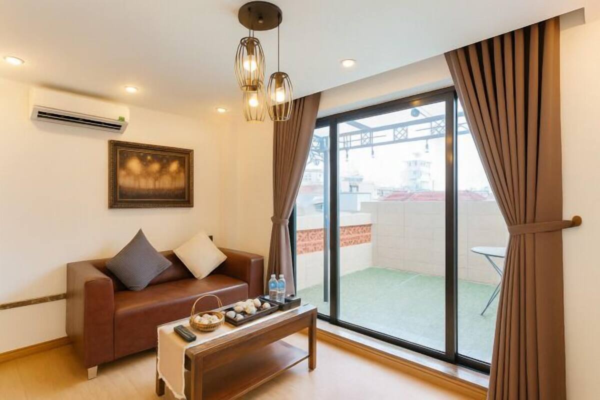 Un salón con un sofá, una mesa de centro con objetos, un cuadro y un amplio ventanal corredero a un área exterior.
