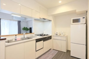 A modern kitchen with white cabinetry, a microwave, a sink, and a dishwasher. - Ito House (Tokyo)