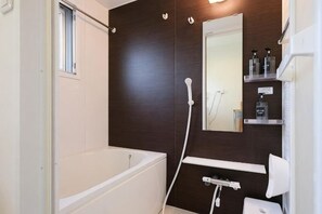 A bathroom with a bathtub, a shower, a mirror, and a shelf with toiletries. - Ito House (Tokyo)