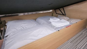 A bed with white linens and a wooden frame, a headboard, and a mattress under a dark ceiling.