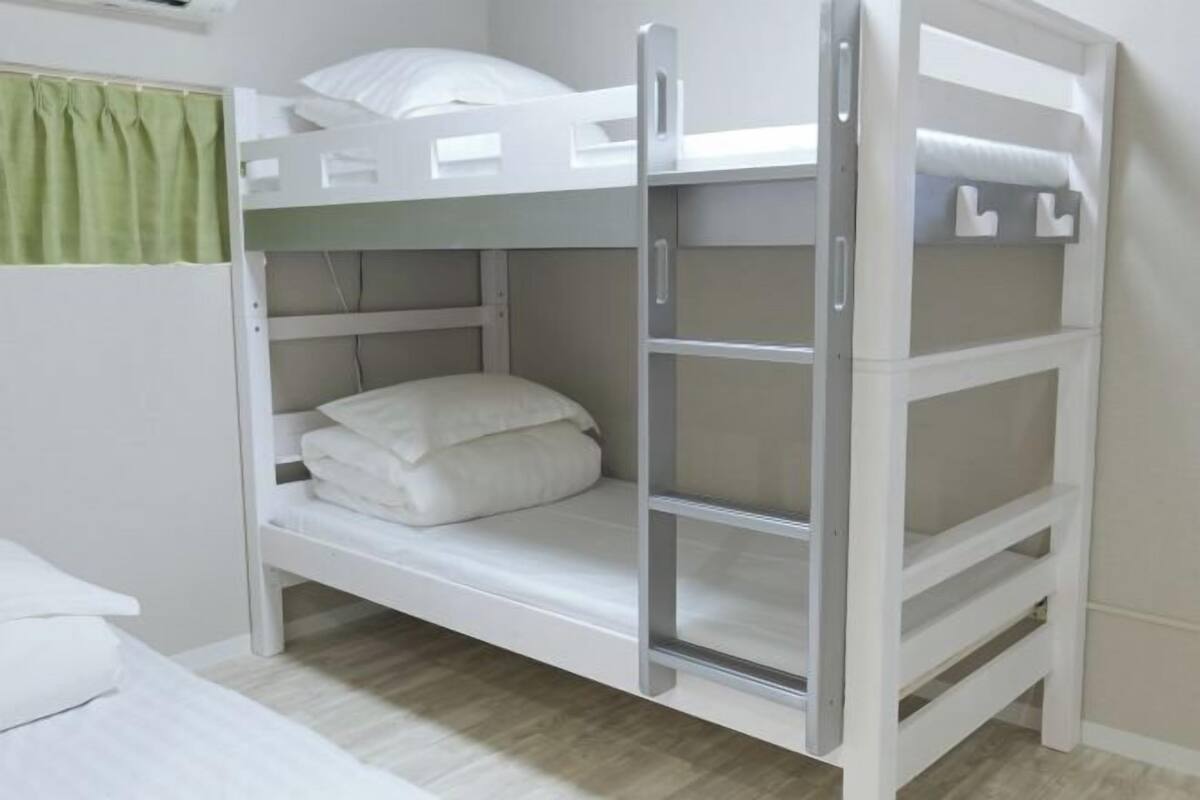 A bunk bed with a pull-out desk, white bedding, and a green curtain.
