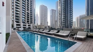 A rooftop pool with lounge chairs, surrounded by high-rise buildings. - bnbme Luxury Apt Pool w/ Burj Khalifa Views (Dubai)