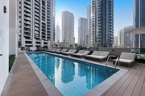 Une piscine sur le toit, dotée de chaises longues et offrant une vue sur les gratte-ciel.