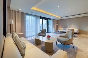 Une chambre d’hôtel moderne, dotée d’un canapé, de fauteuils, d’une table basse et d’une grande fenêtre avec des rideaux.