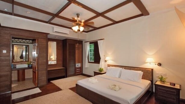 A bedroom with a large bed, a ceiling fan, a nightstand, a mirror, and a window with curtains. - Sipadan Mabul Resort Semporna (Semporna)