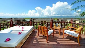 A balcony with a mattress, wooden chairs, and a table.