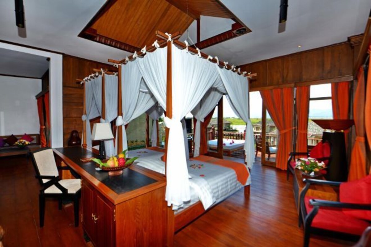 A spacious bedroom with a large bed, a desk with a fruit bowl, and a view of the outdoors.