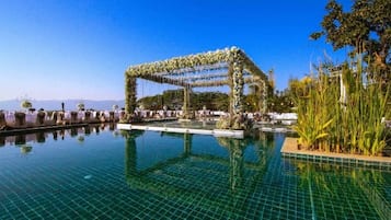 A clear blue sky, a swimming pool with a tiled surface, and a structure with a floral archway.