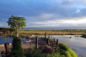 A pool area with a wooden deck, surrounded by lush greenery and a view of a river. - Aureum Palace Hotel and Resort Inle (Taunggyi)