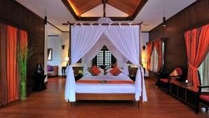 A spacious room with a large bed, wooden flooring, and a high ceiling with a wooden beam structure.