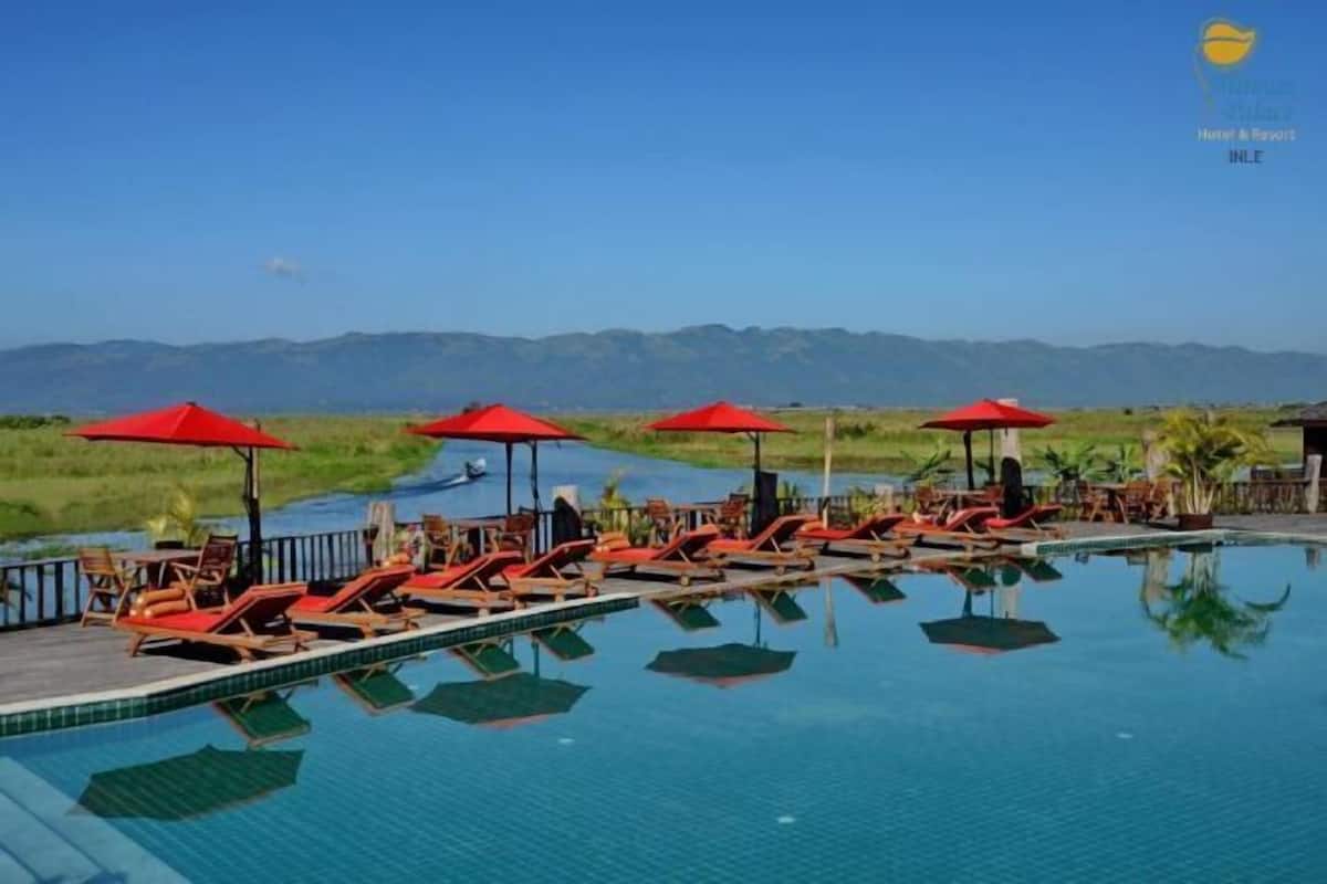 Zona junto a la piscina con sillones de descanso y sombrillas rojas, rodeada de un paisaje natural y montañas al fondo.