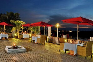 An outdoor dining area with tables and chairs, red umbrellas, and a fire pit. - Aureum Palace Hotel and Resort Inle (Taunggyi)