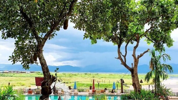 A pool area with lounge chairs, a hammock, and a view of the beach and mountains.