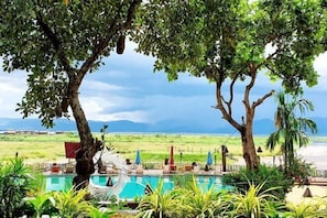 A pool area with lounge chairs, a hammock, and a view of the beach and mountains. - Aureum Palace Hotel and Resort Inle (Taunggyi)