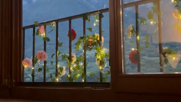 Et værelse med udsigt til bjerge gennem et vindue med gelænder pyntet med blomster og lys.