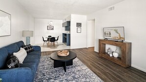 Un saló modern amb un sofà blau, una taula de centre rodona i un moble de consola de fusta amb un televisor.