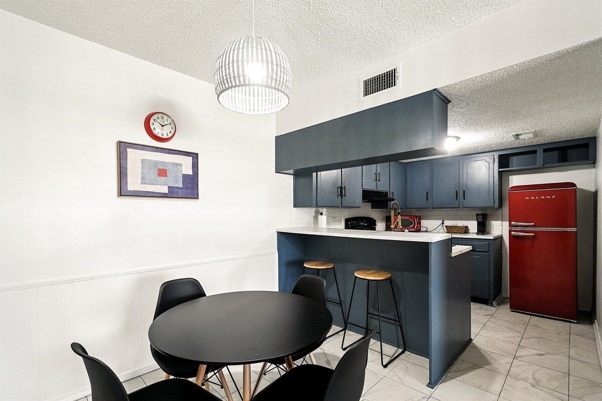 Una cocina moderna con una isla central, taburetes de bar y un refrigerador rojo.