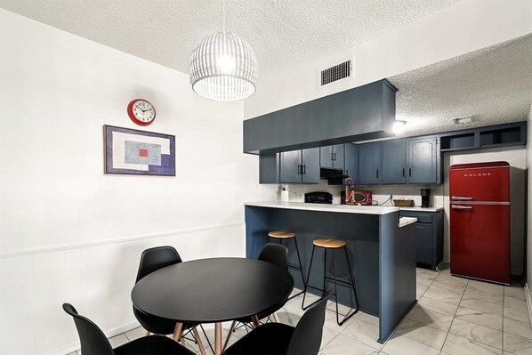 A modern kitchen with a central island, bar stools, and a red refrigerator.