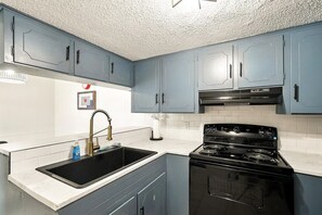 A kitchen with blue cabinets, a black stove, and a white countertop.