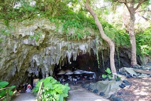 A cave entrance with a wooden pathway leading inside, surrounded by greenery and trees. - kafuya tsukishiro (Nanjo)