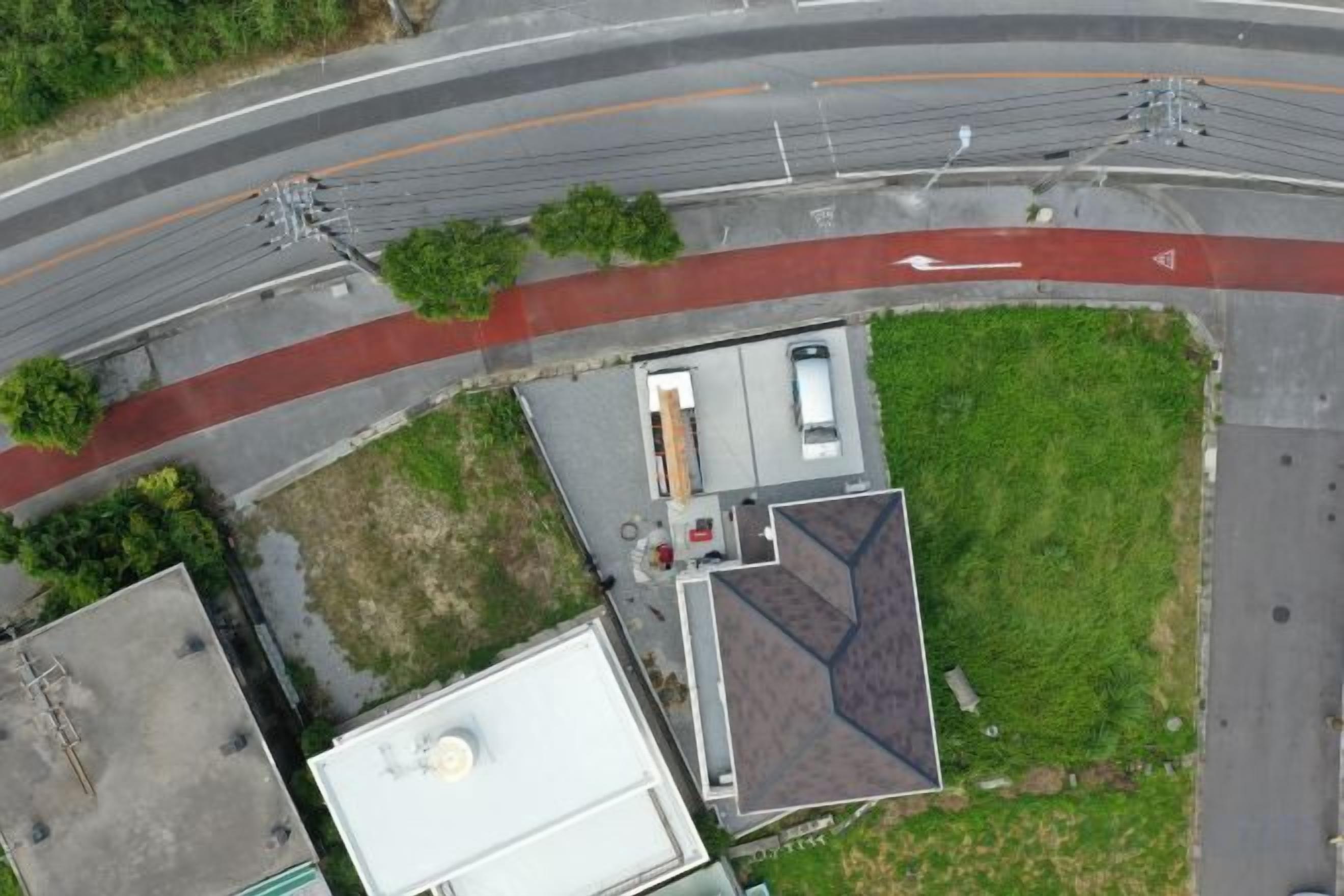 An aerial view of a building with a flat roof, a parking area, and a red pathway.