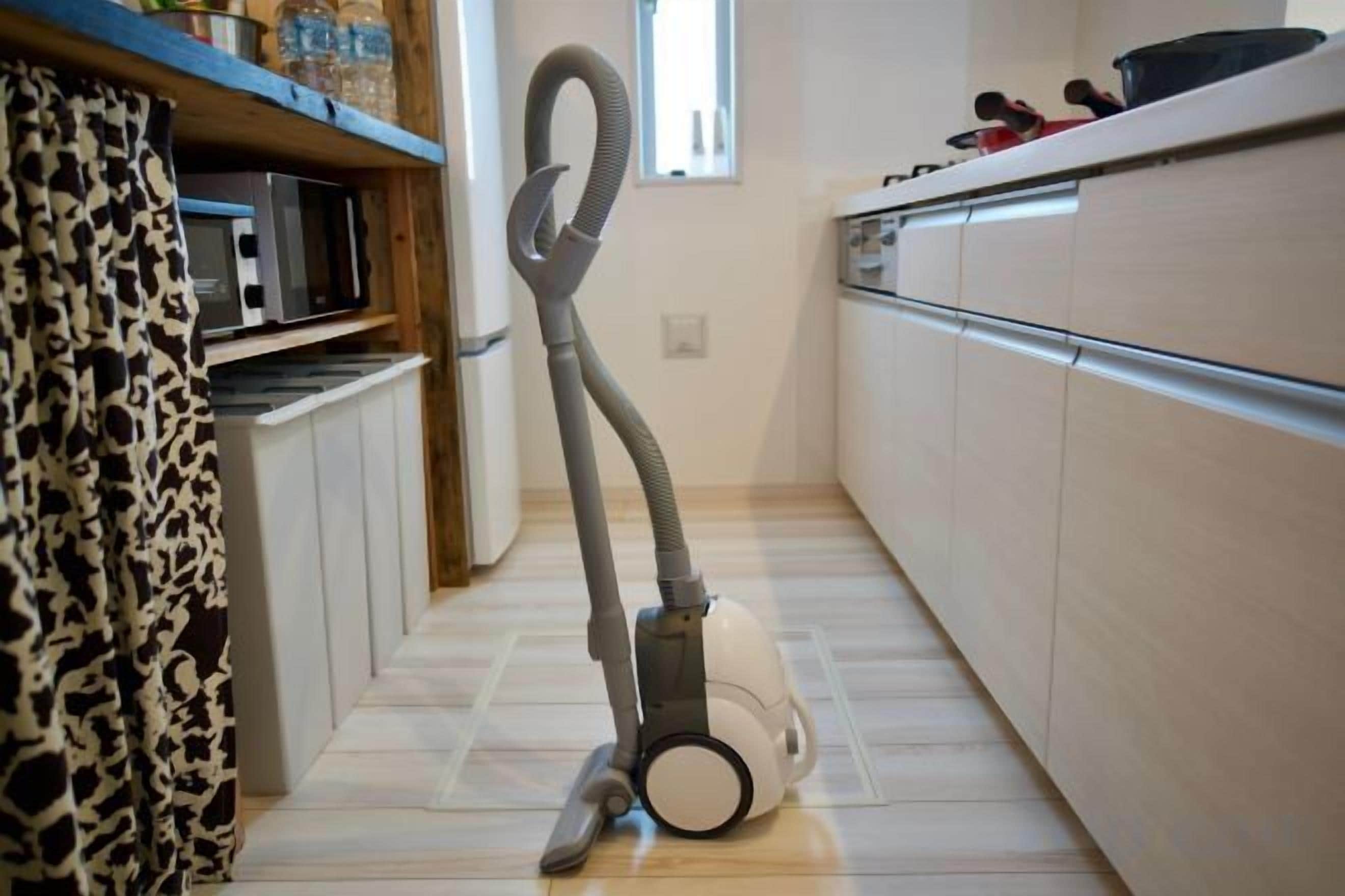 A kitchen with a vacuum cleaner, a microwave, and a refrigerator.