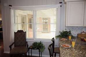 A kitchen with white cabinets, a granite countertop, and a window with blinds.