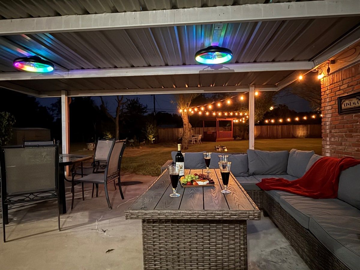 An outdoor patio with a dining table set for two, a wicker coffee table, and a sofa with cushions.