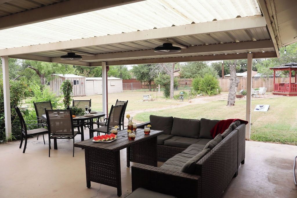 Une terrasse extérieure dotée d’un espace salon couvert, d’une table avec des boissons et d’une vue sur le jardin arrière.
