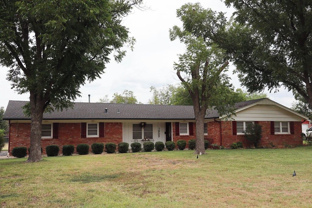 A single-story brick house with a front porch, a garage, and a lawn.