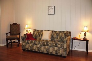 A room with a patterned sofa, a wooden chair, two lamps, and a wall-mounted sign.