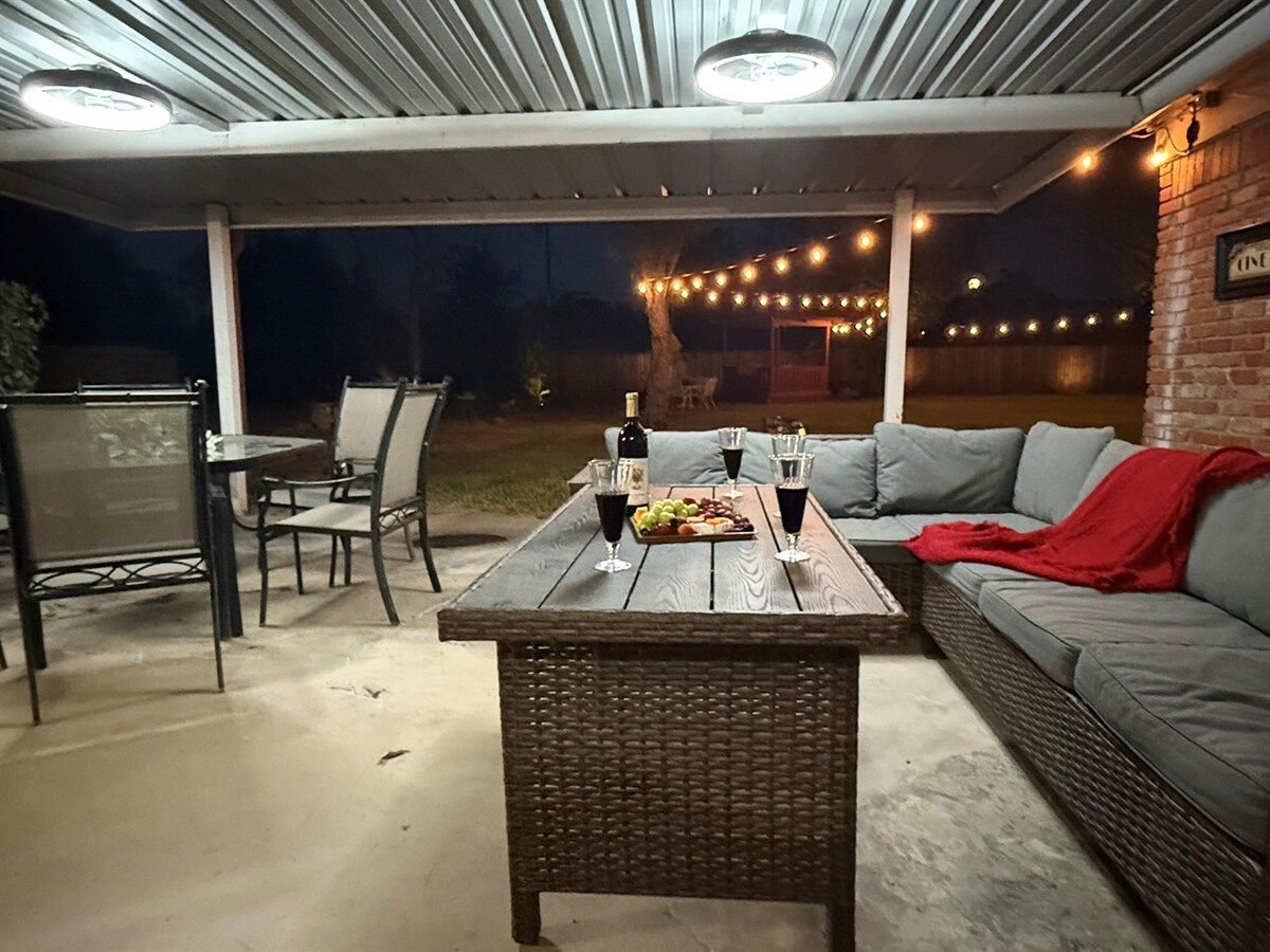 Une terrasse extérieure avec une table dressée pour le repas, des chaises, un canapé et des guirlandes lumineuses.