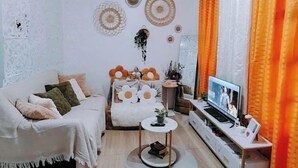 Ein Wohnzimmer mit einer Couch, einem Couchtisch, einem Fernseher und orangefarbenen Vorhängen.