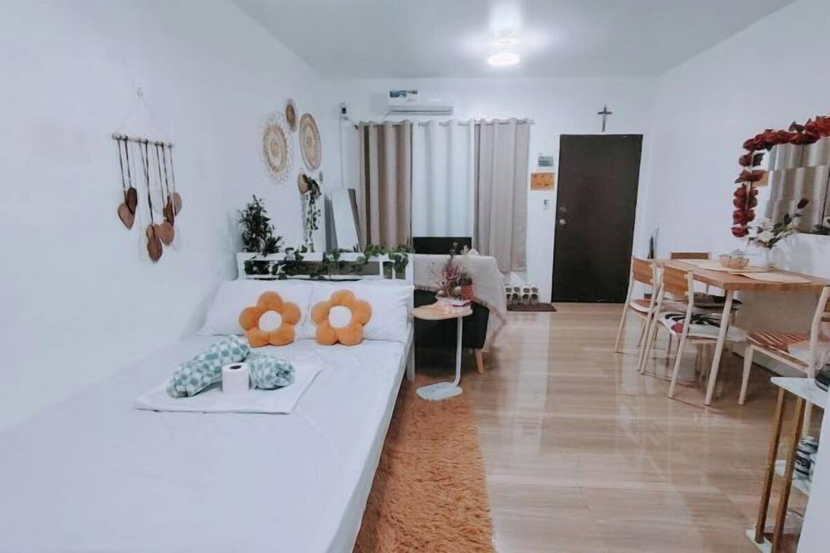A living room with a sofa, a dining table with chairs, a small side table, and a door with a cross.