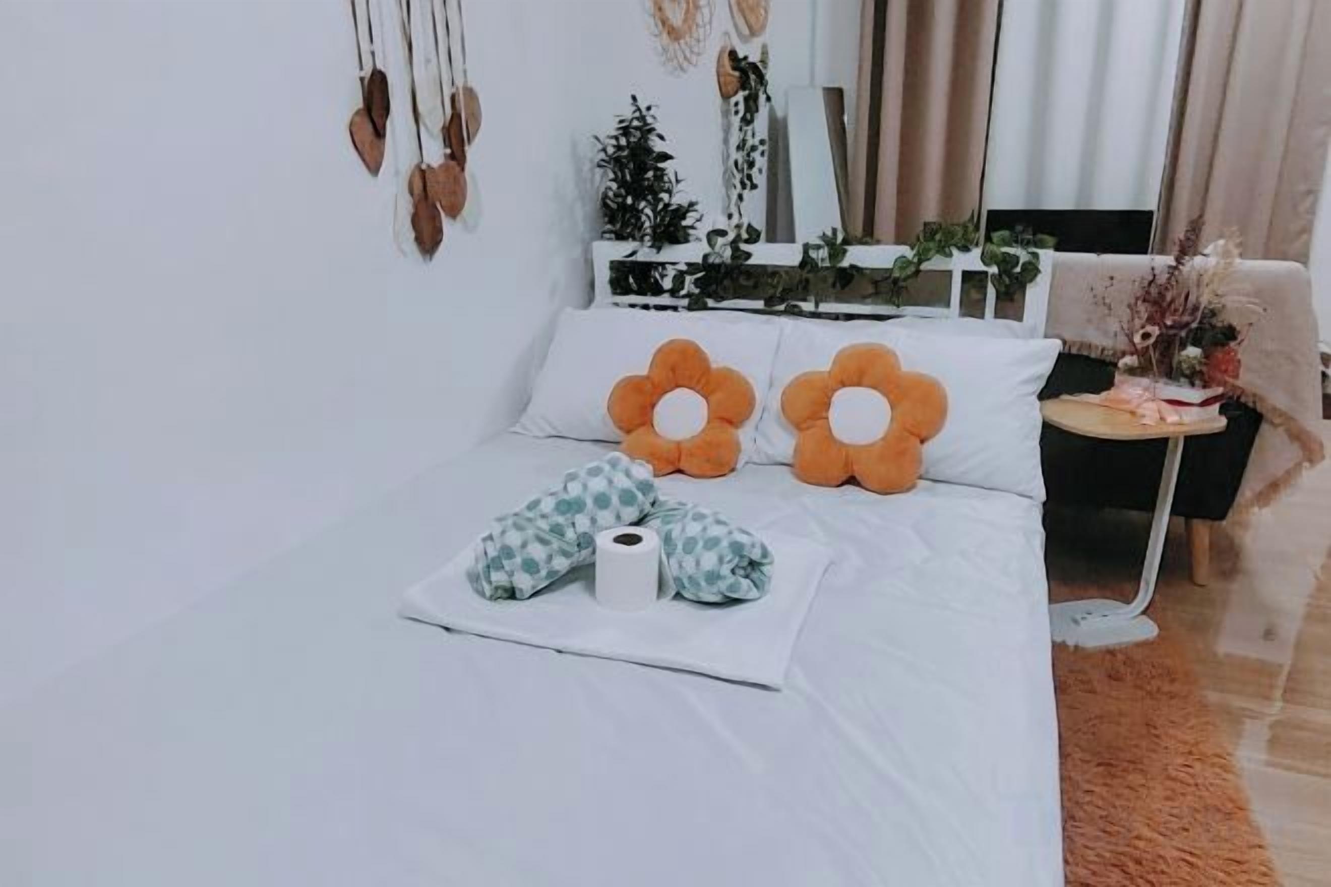 A neatly made bed with two orange flower-shaped pillows, a white blanket, and a checkered pillow.