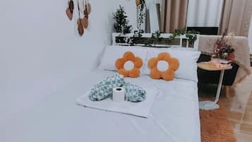 A neatly made bed with two orange flower-shaped pillows, a white blanket, and a checkered pillow.