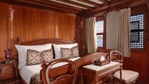 A wooden-paneled room with a bed, two chairs, a nightstand, and a window with curtains. - Dahabeya Farouz El Nil 3 (Al Bairat)
