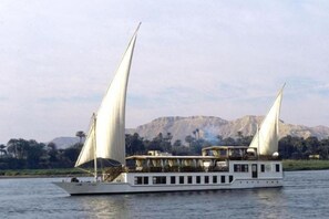 A white riverboat with two sails, a covered deck, and a mountainous backdrop. - Dahabeya Farouz El Nil 3 (Al Bairat)